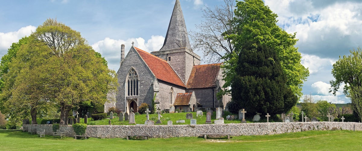 A church with a tall steeple and a stone wall surrounding the graveyard.