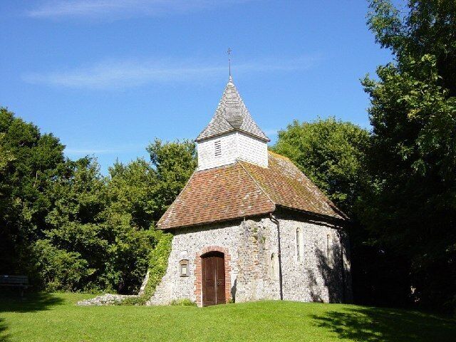 A small stone church with a red-tiled roof and a bell tower, surrounded by lush green trees.