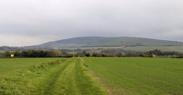 Footpath between Berwick and Alfriston Road Windover Hill in the distance - with the Long Man of Wilmington just out of view. The yellow object on the left is a bouncy castle at Drusilla's Zoo.