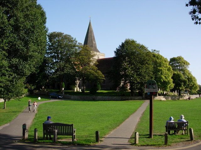 A church with a tall steeple, a grassy park with a walking path, and benches.