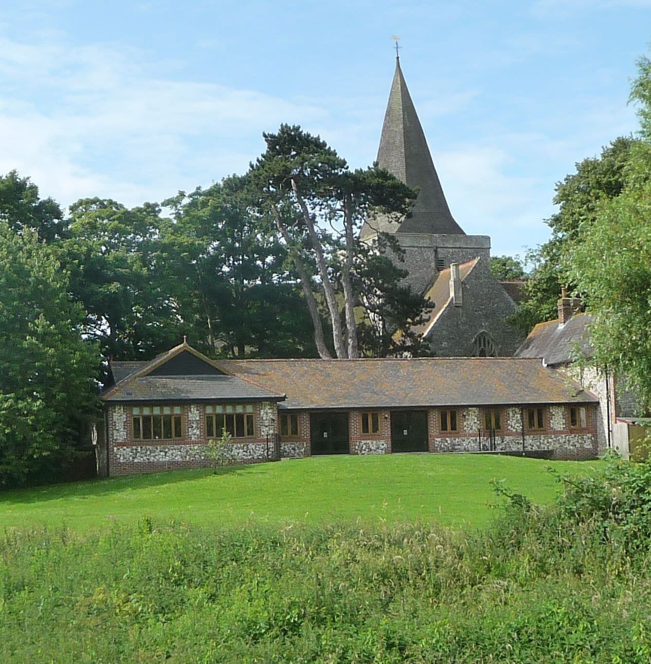 A church with a tall steeple, surrounded by trees and a grassy field.