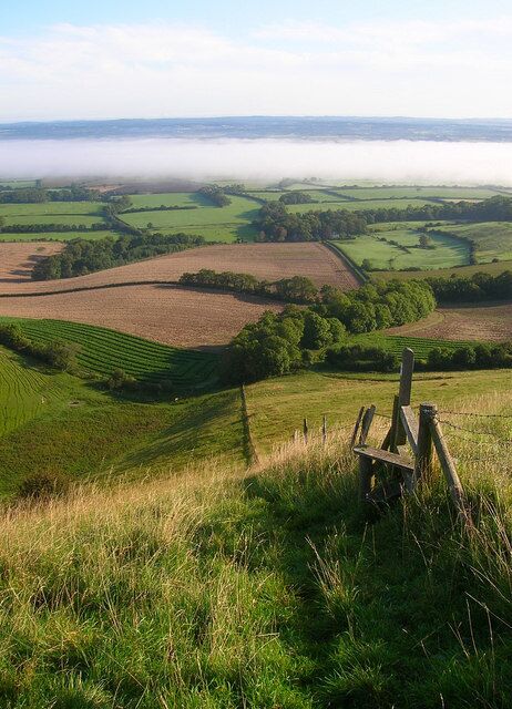 Rolling green hills, a wooden fence, and a distant fog-covered valley.