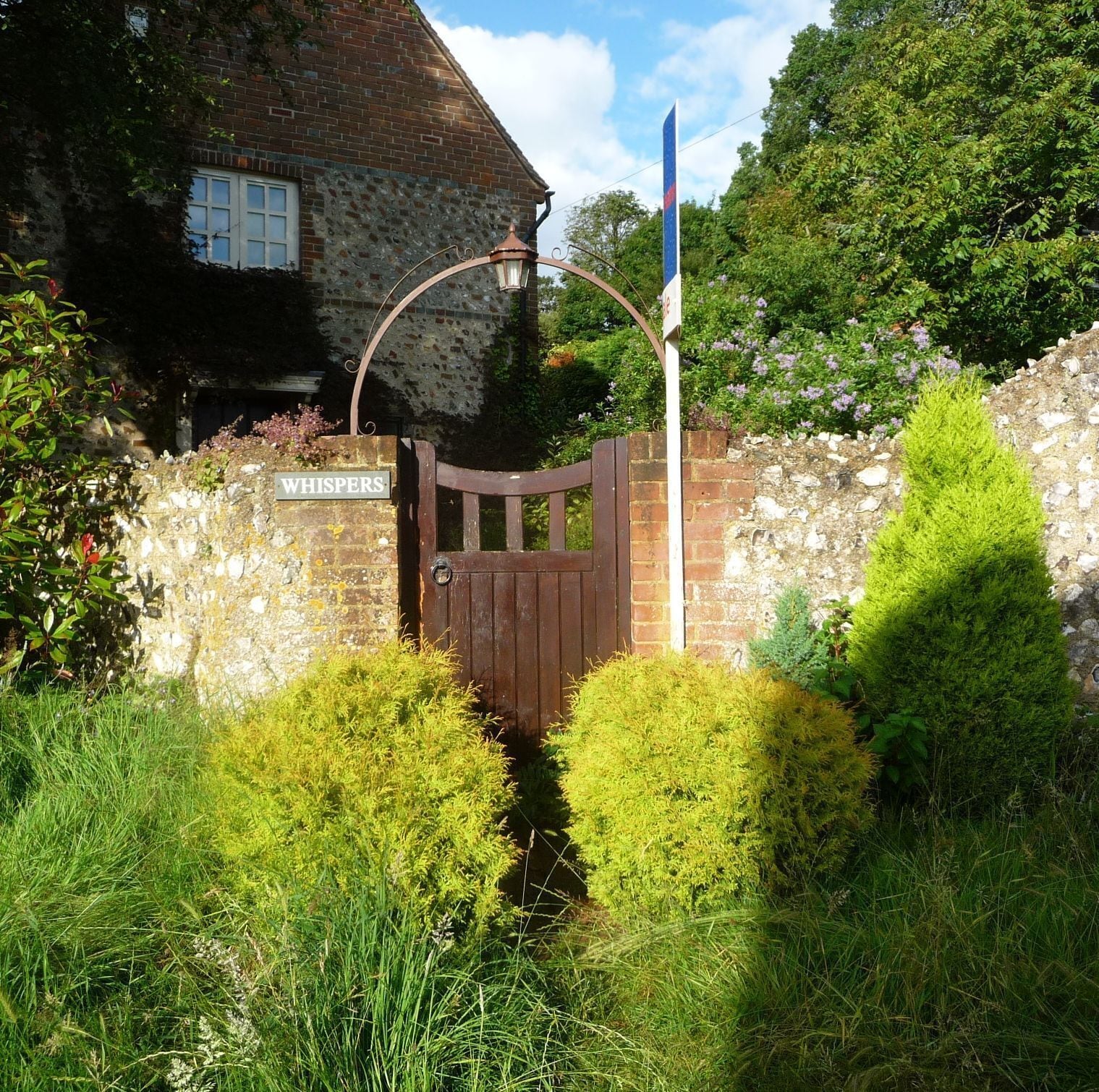 A stone wall, a wooden gate, and a sign that reads "WHISPERS".
