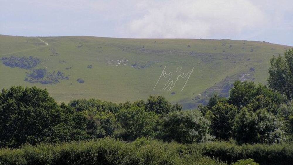 A green hill with a path and some trees in the foreground.