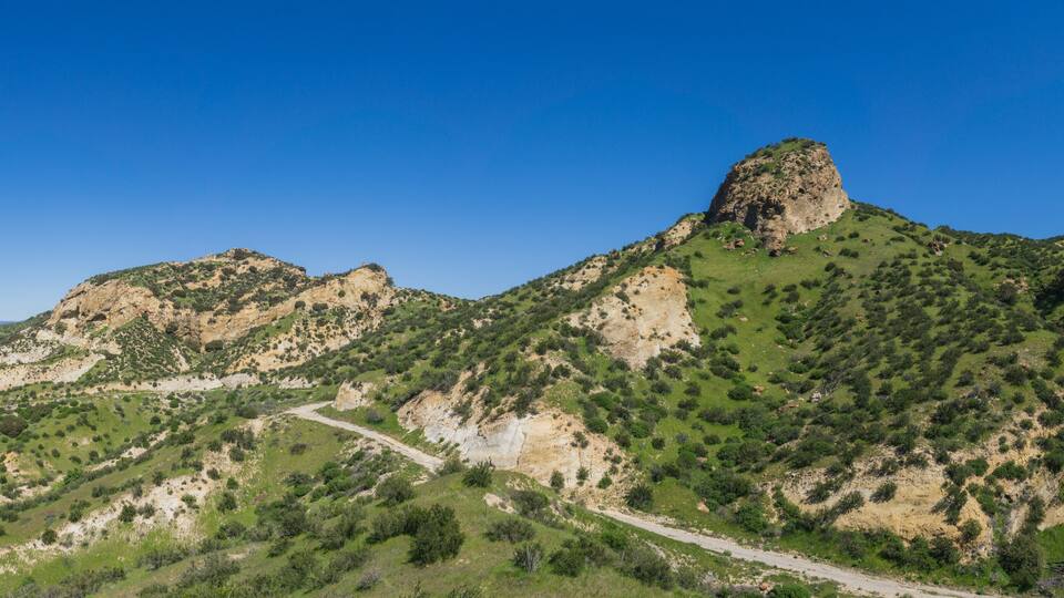 A mountainous landscape with a prominent rocky peak and a winding road.