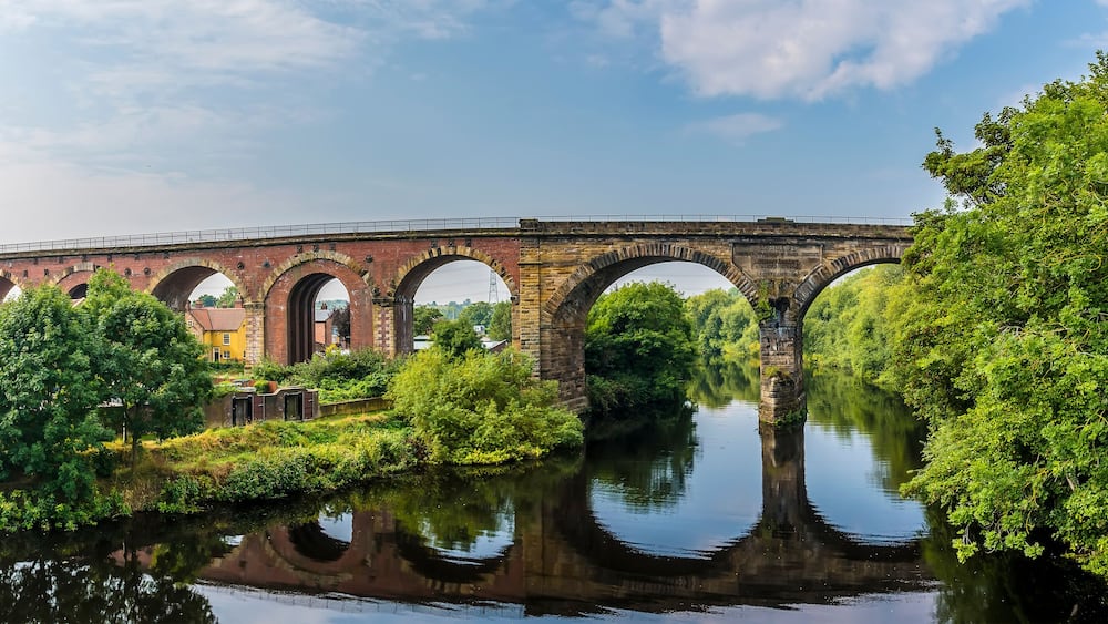 Un pont de pierre à arches multiples enjambant une rivière, entouré d’une végétation luxuriante et d’arbres.