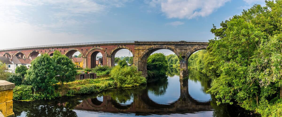 A stone bridge with multiple arches spanning a river, surrounded by lush greenery and trees.