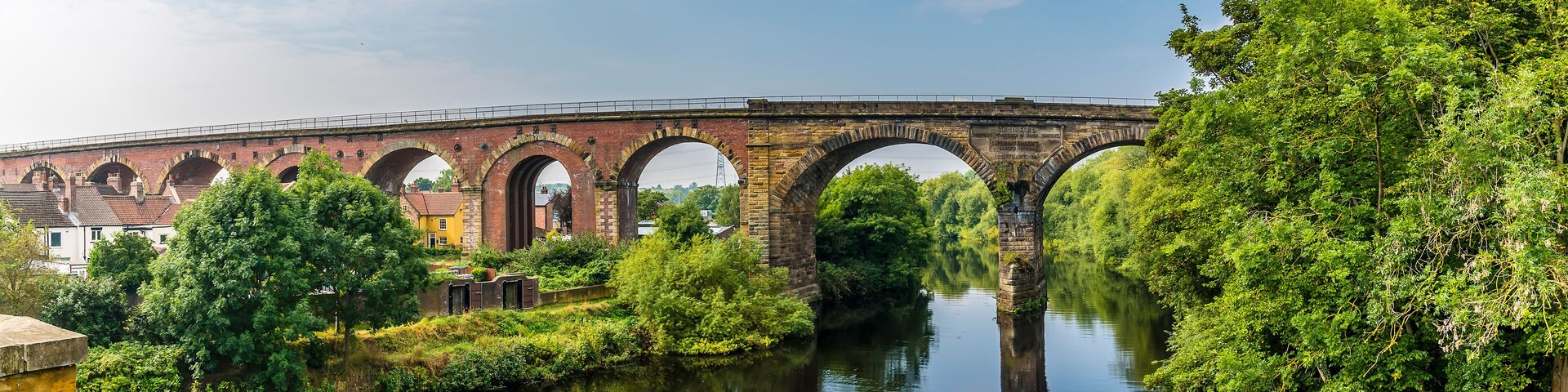 A stone bridge with multiple arches spanning a river, surrounded by lush greenery and trees.