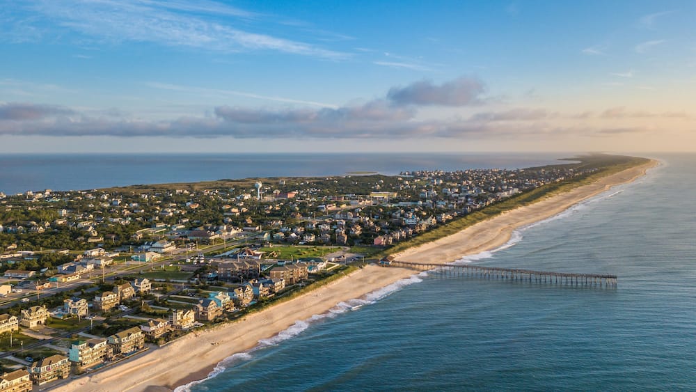 Une ville côtière avec une plage, des maisons et une jetée qui s’avance dans l’océan.