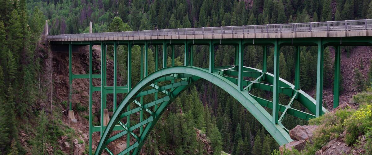 A green metal bridge spanning a deep gorge with steep, forested cliffs.