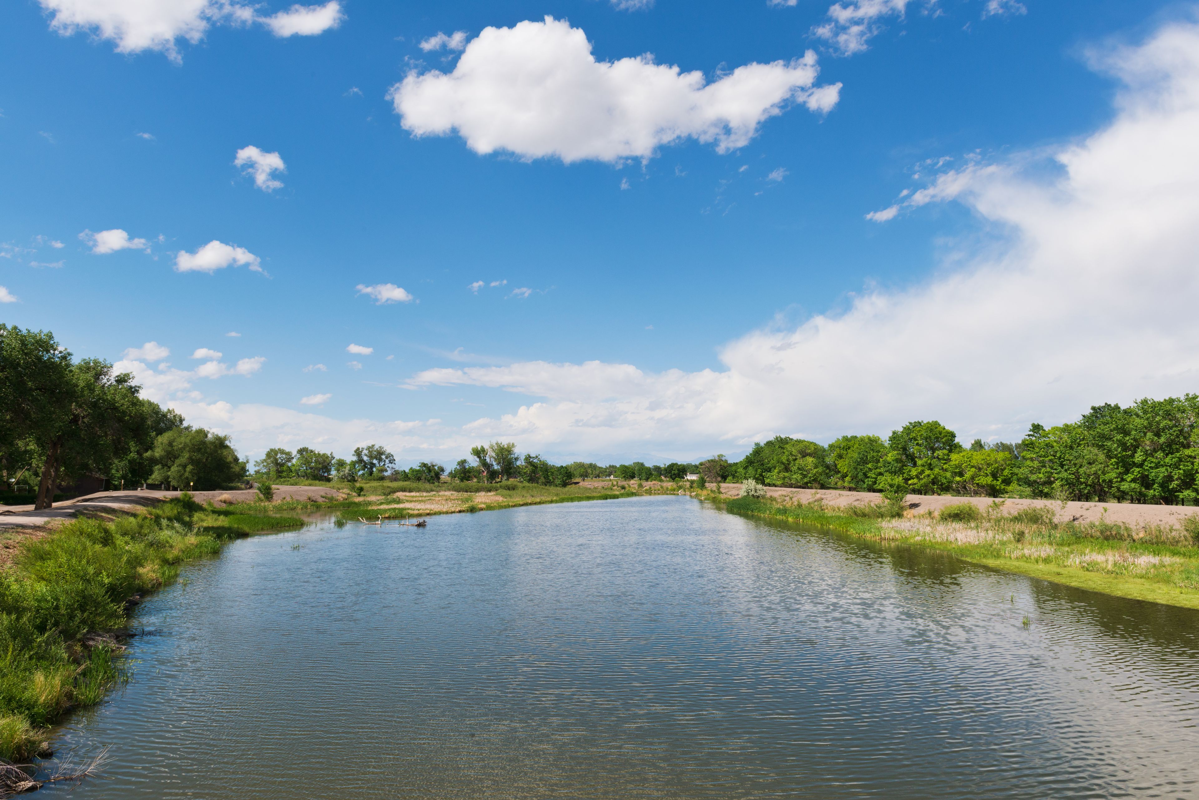 A calm river with a clear sky and scattered clouds.