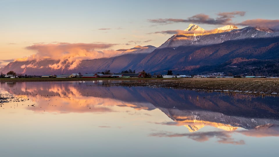 A mountain range with a lake reflecting the scenery, including a small village and a prominent peak.