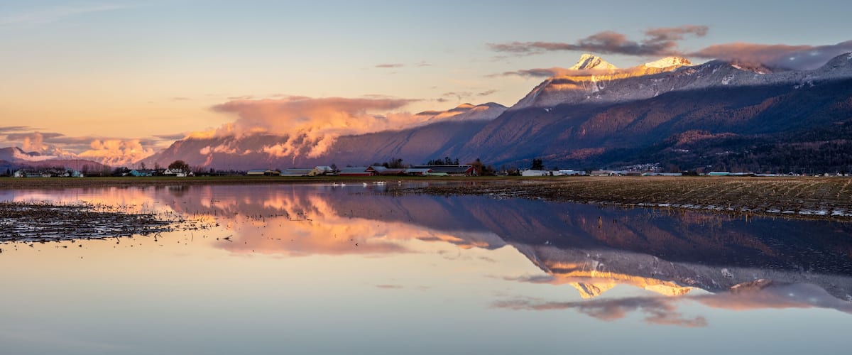 A mountain range with a lake reflecting the scenery, including a small village and a prominent peak.