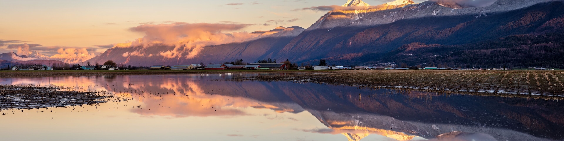 A mountain range with a lake reflecting the scenery, including a small village and a prominent peak.