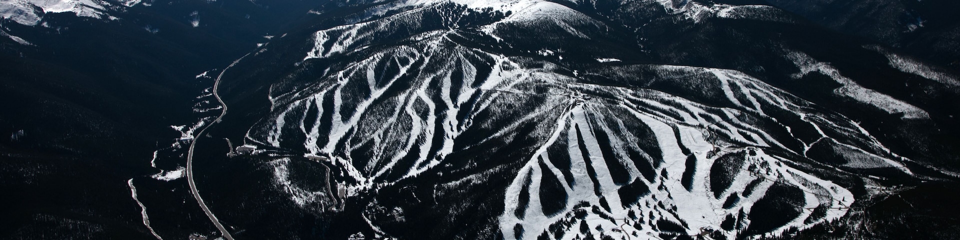 A snow-covered mountain range with distinct ridges and valleys, a winding road, and a clear blue sky.