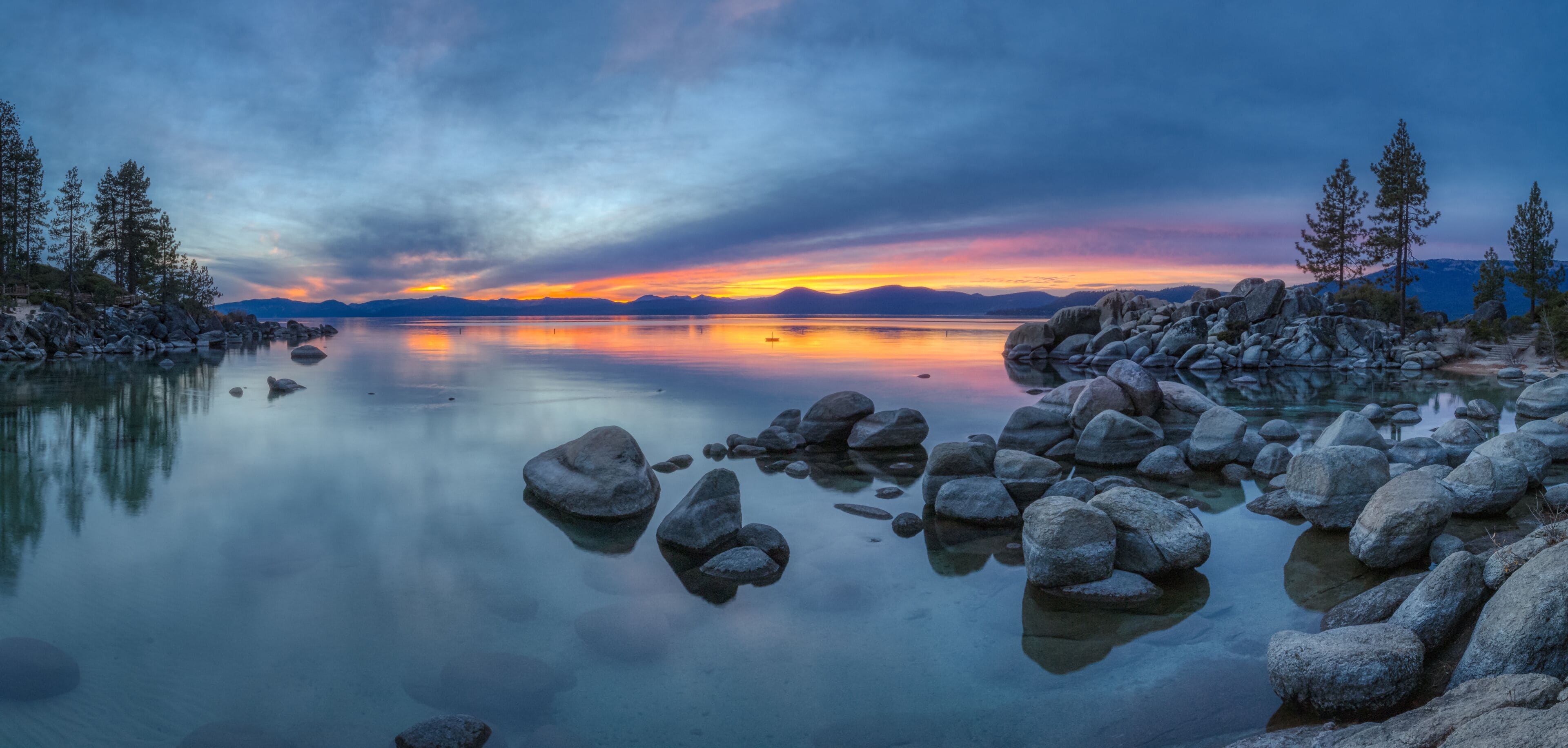 Um lago calmo com pedras grandes em primeiro plano e um pôr do sol ao fundo.