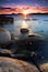 A sunset over a calm lake with rocks in the foreground.