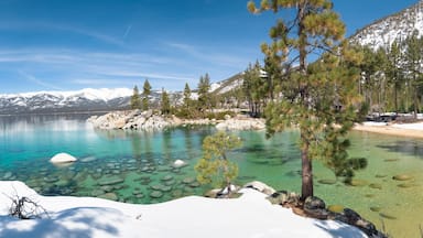 A clear lake surrounded by snow-capped mountains and pine trees.