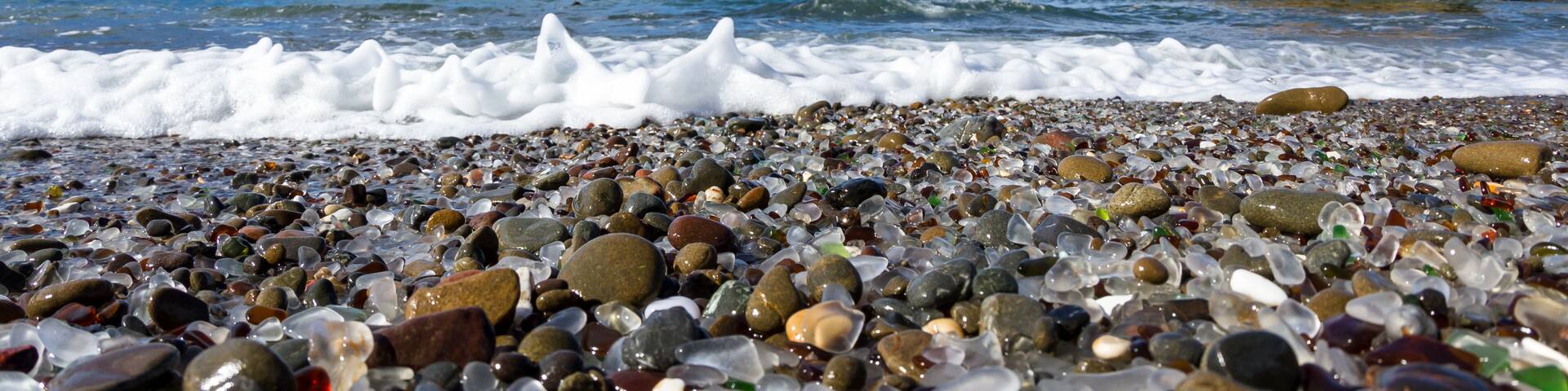 A pebble beach with waves, clear sky, and rocky formations.