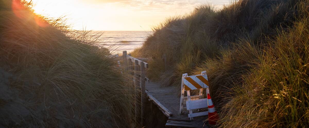 Hazard signs block boardwalk leading to beach during golden sunset