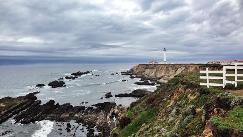 A rocky coastline with a lighthouse and white fence.