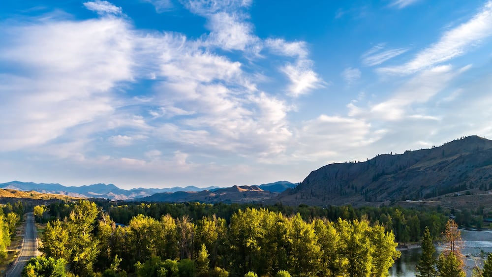 A mountainous landscape with a river, dense forest, and a clear sky.