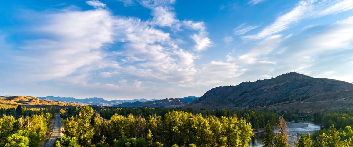 A mountainous landscape with a river, dense forest, and a clear sky.