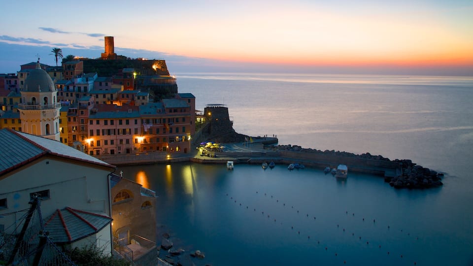 A coastal town at sunset with historic buildings, a fortified tower, and calm waters.