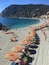 A beach with rows of striped umbrellas and sun loungers, clear blue water, and a mountainous backdrop.