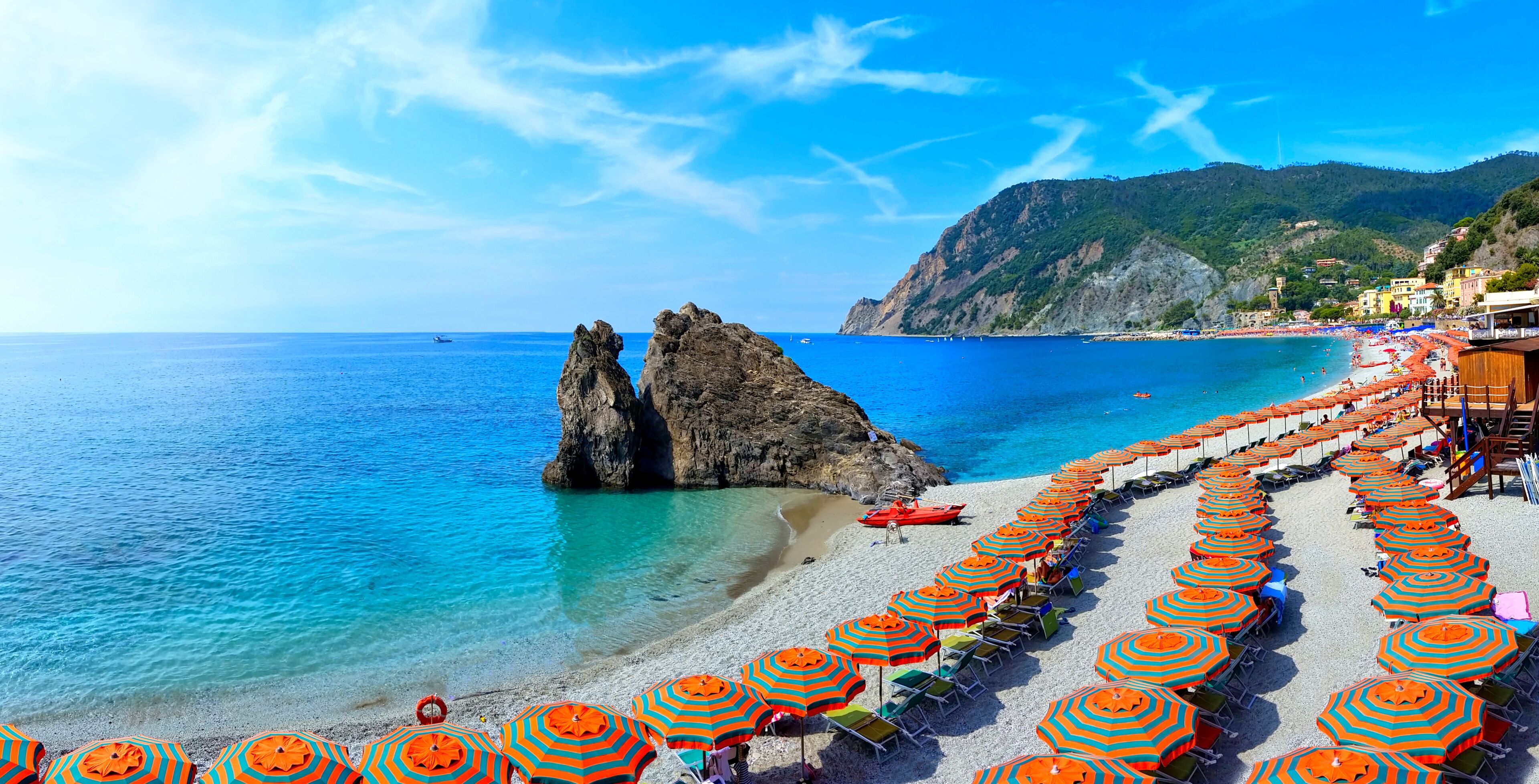 A beach with clear blue waters, rocky formations, and rows of colorful umbrellas.