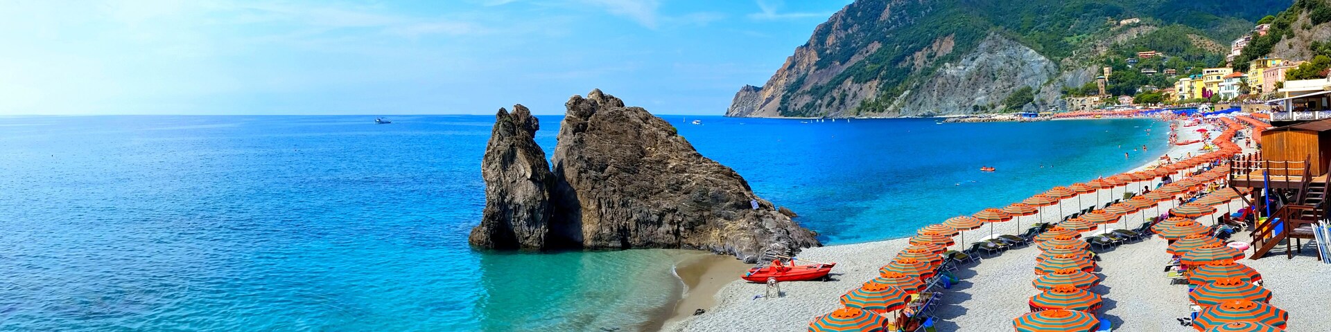 A beach with clear blue waters, rocky formations, and rows of colorful umbrellas.