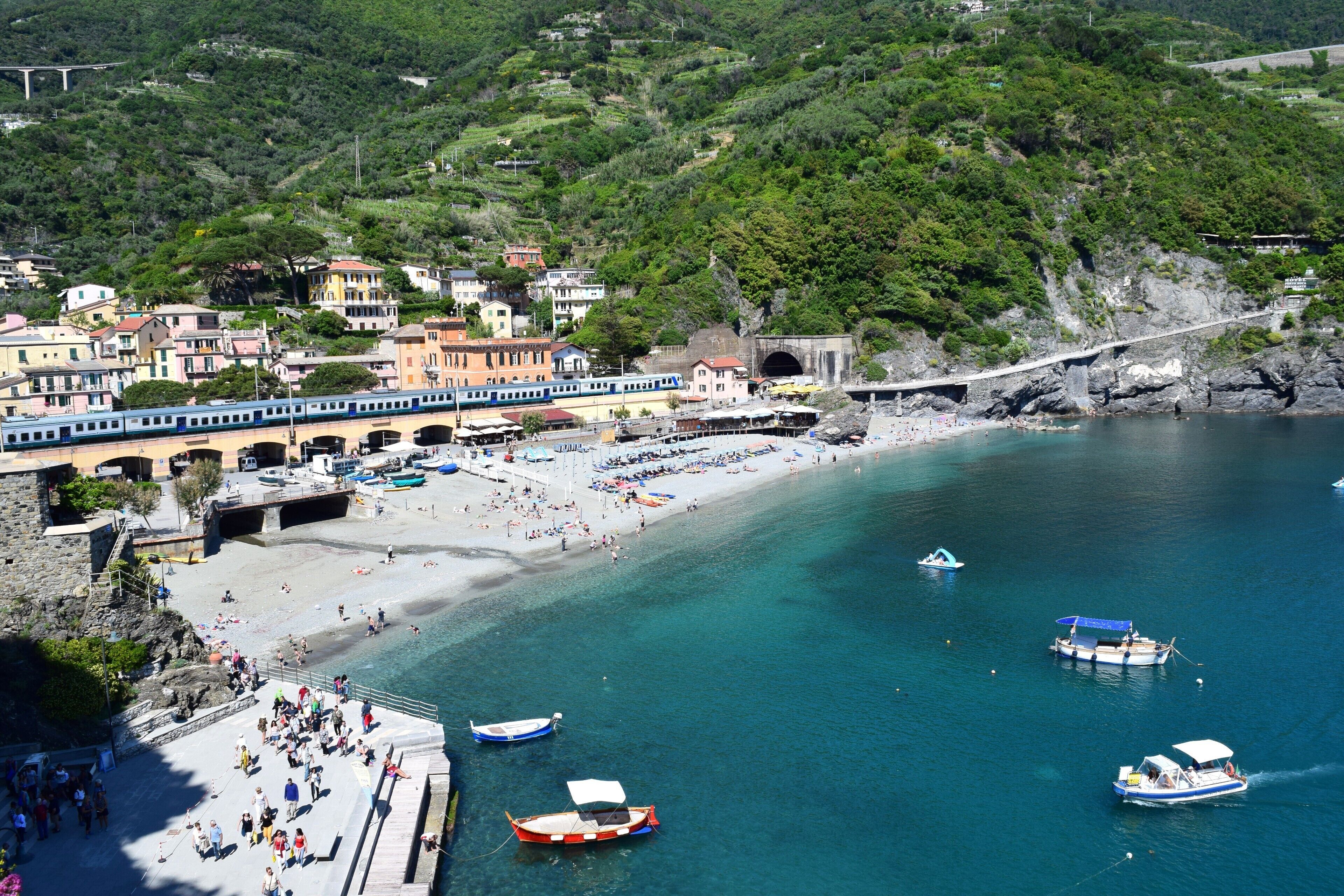 A coastal town with a beach, boats, a train, and a bridge.