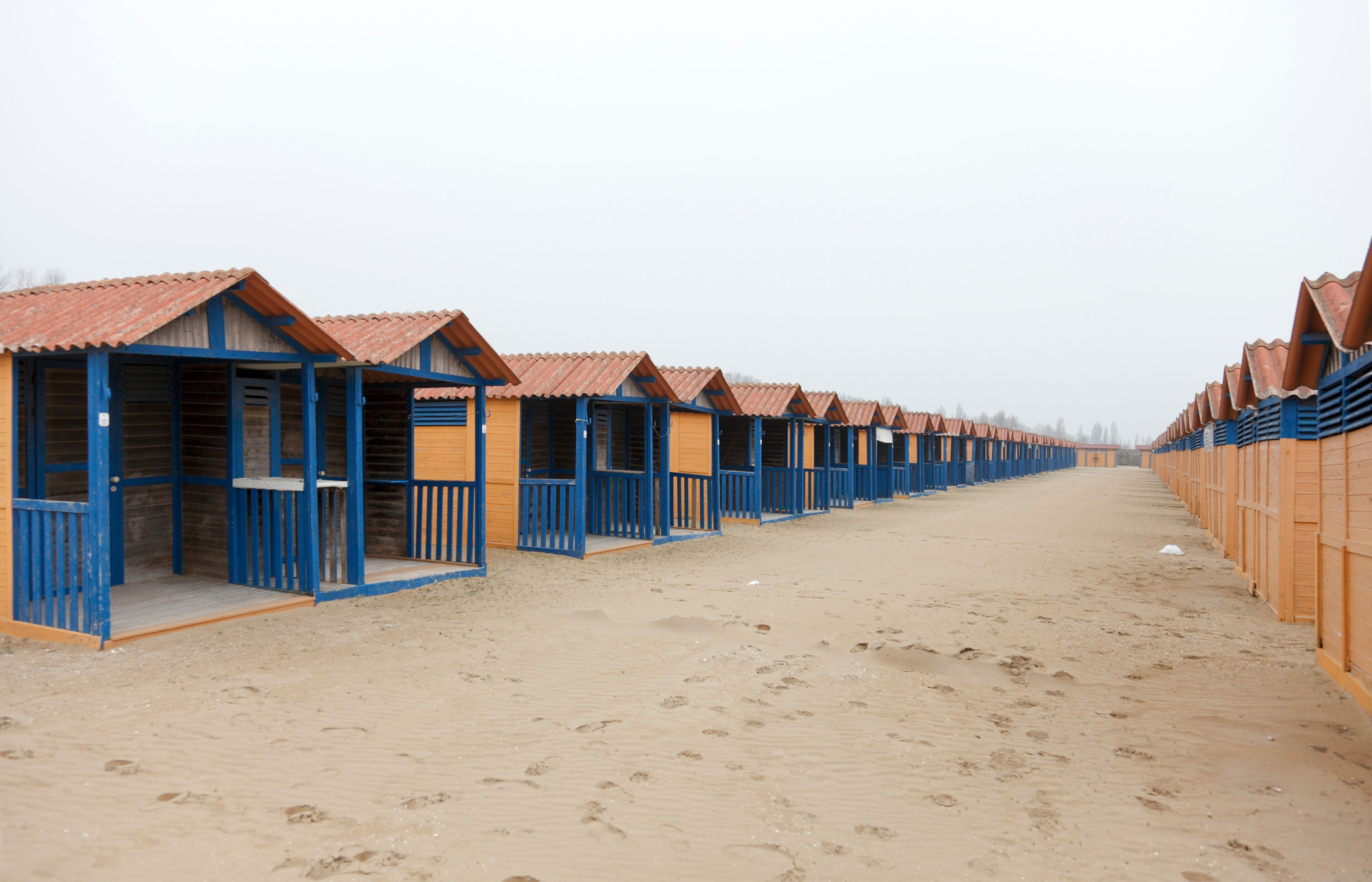 A row of beach huts with blue railings and red roofs.