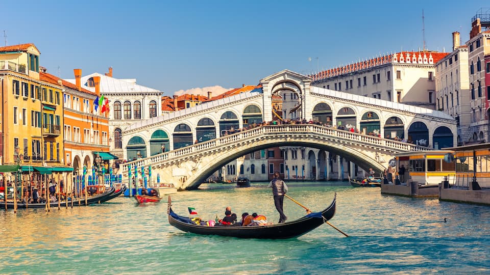 A gondola on a canal in Venice, Italy, with a bridge and historic buildings in the background.