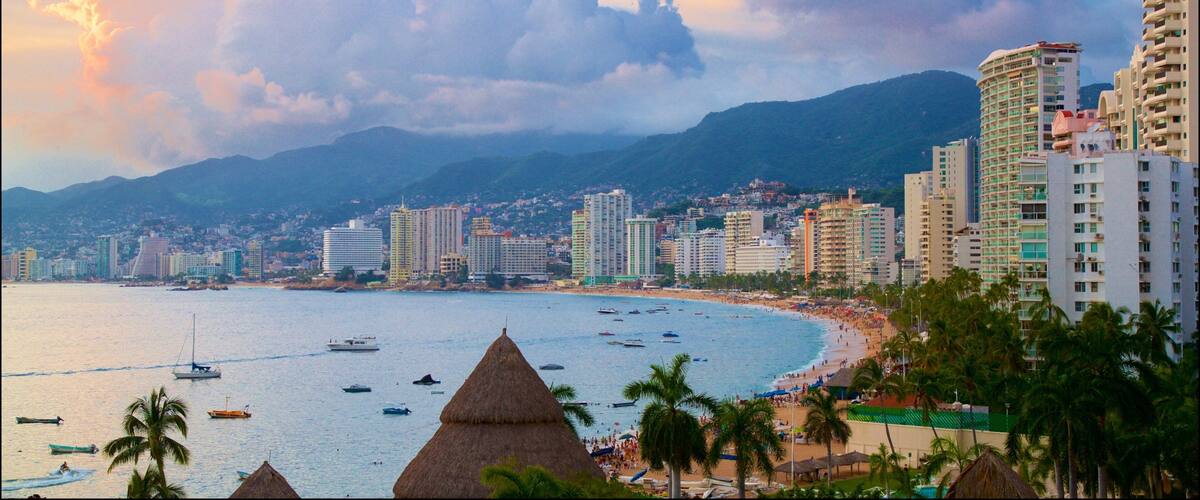 A coastal cityscape with a beach, boats, and palm trees.