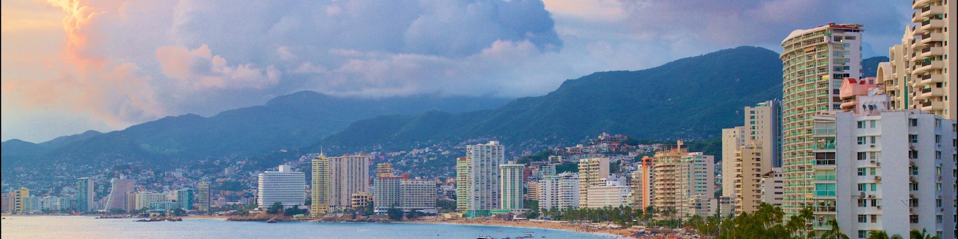 A coastal cityscape with a beach, boats, and palm trees.