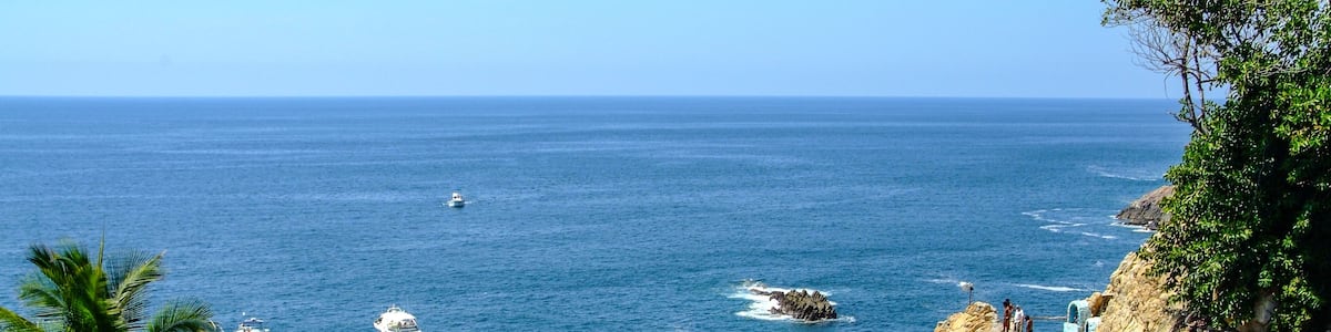 Une zone côtière caractérisée par des falaises rocheuses, un escalier en pierre et des bateaux sur l’eau.