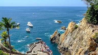 Una zona costera con acantilados rocosos, una escalera de piedra y barcos en el agua.
