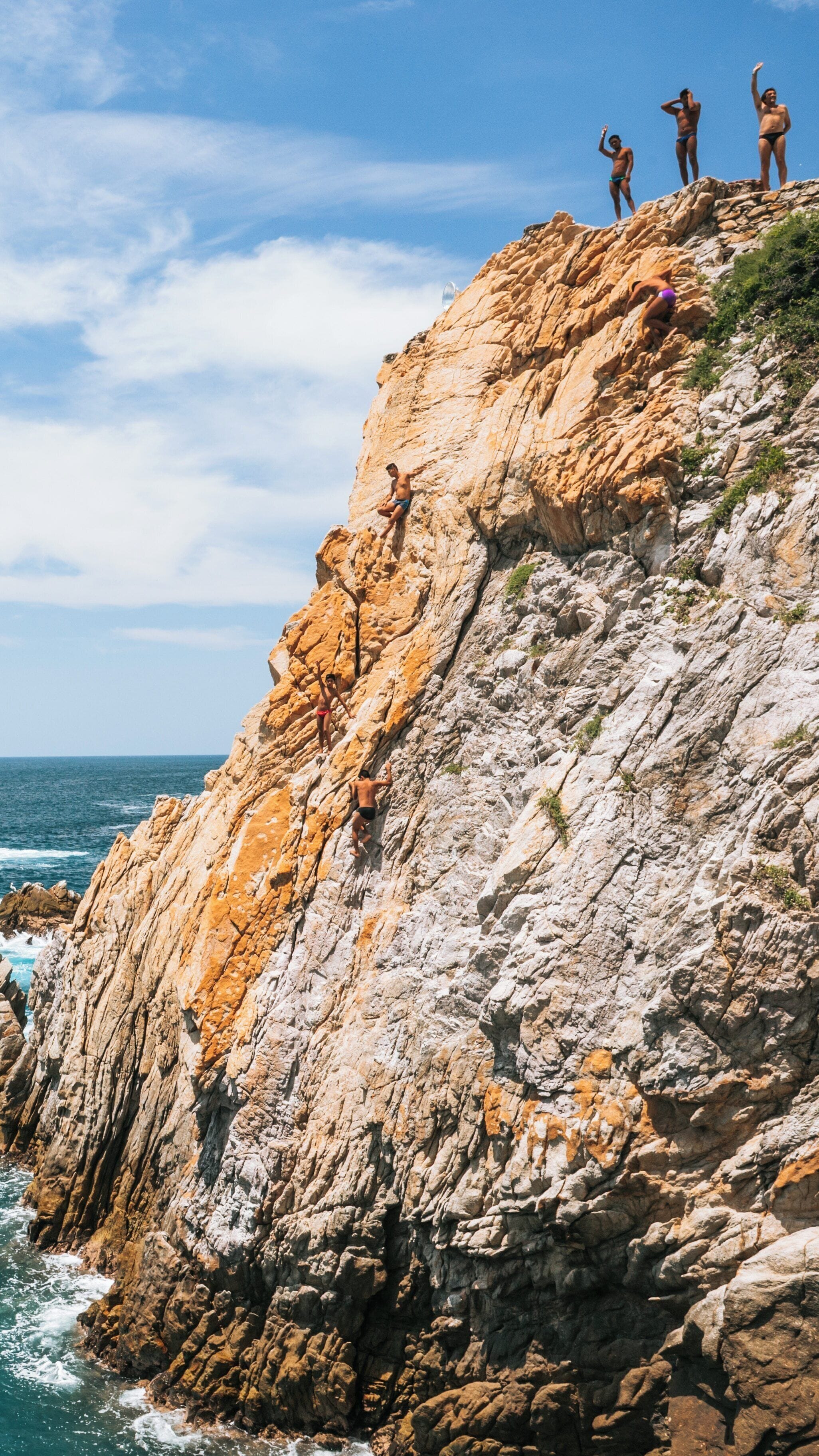 Cliff divers showcasing their skills at La Quebrada Cliffs in Las Playas, Acapulco, Guerrero, Mexico under a bright sunny sky