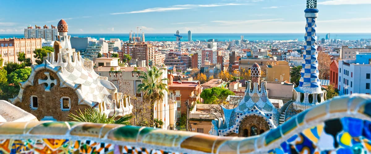 A panoramic view of a city with distinctive modern architecture, including a famous building with a mosaic roof and a tower with a checkered pattern.