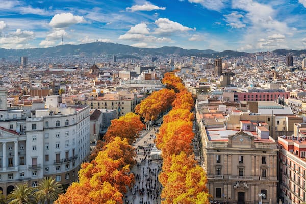A cityscape with autumn foliage, a prominent building with a clock tower, and a distant mountain range.
