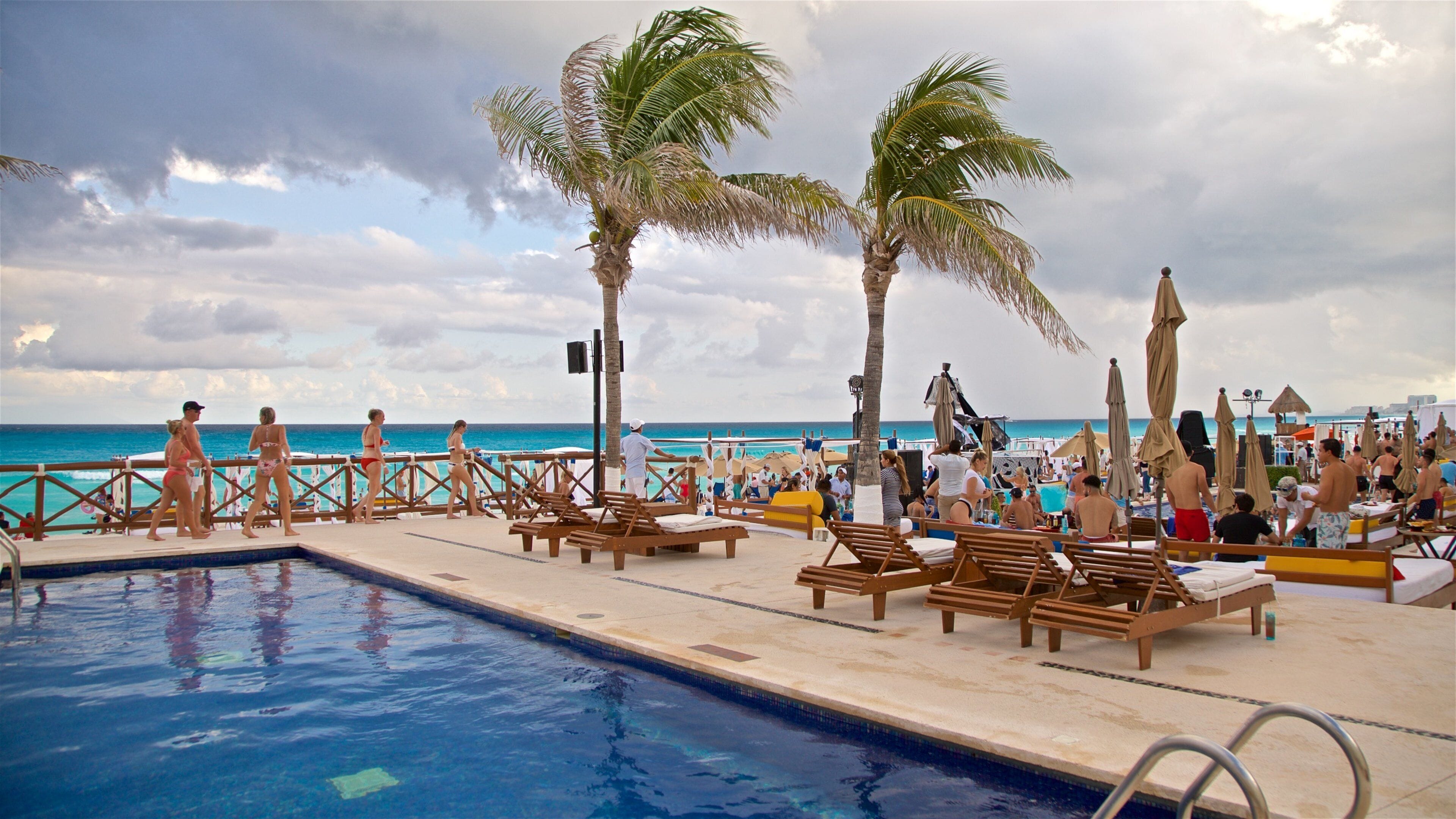 A poolside area with lounge chairs, palm trees, and a view of the ocean.