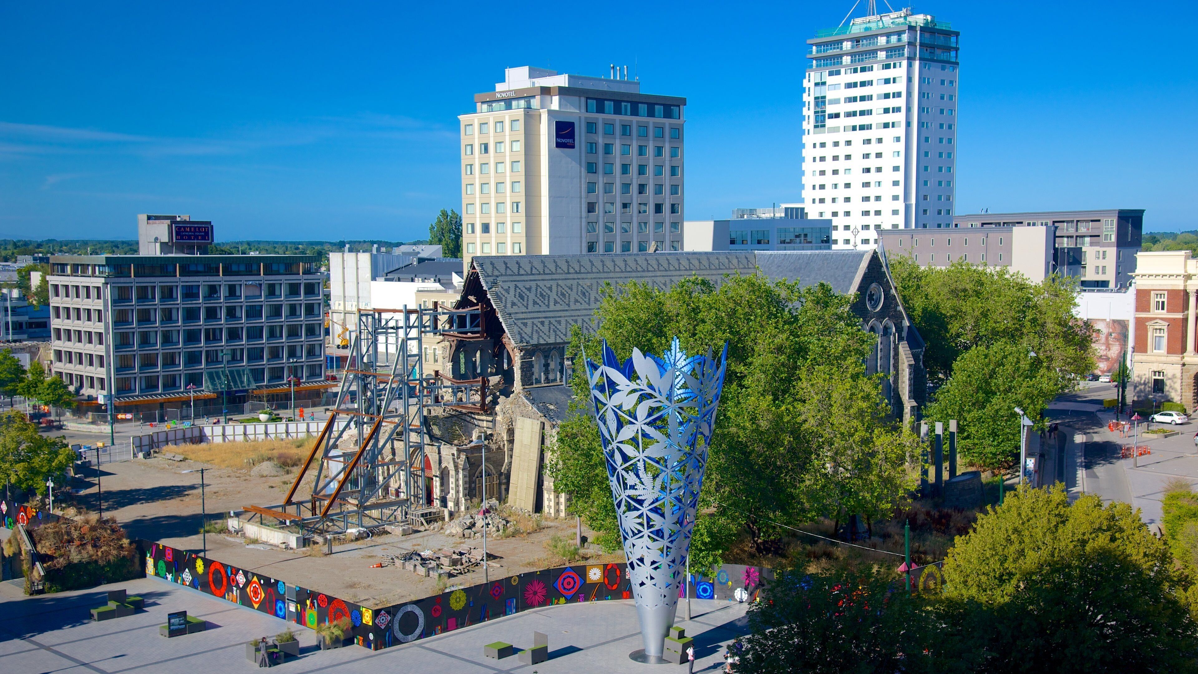 A cityscape with modern buildings, a construction site, and a distinctive blue sculpture.