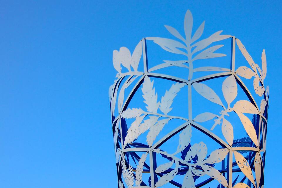 A metal sculpture with leaf patterns against a clear blue sky.