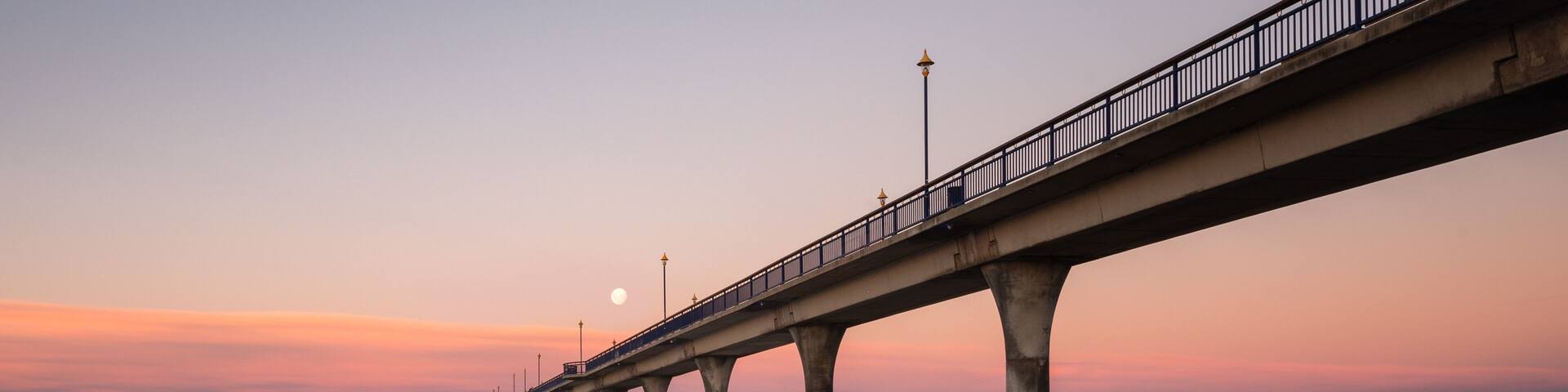 A pier extending into calm waters at sunset with a clear sky.