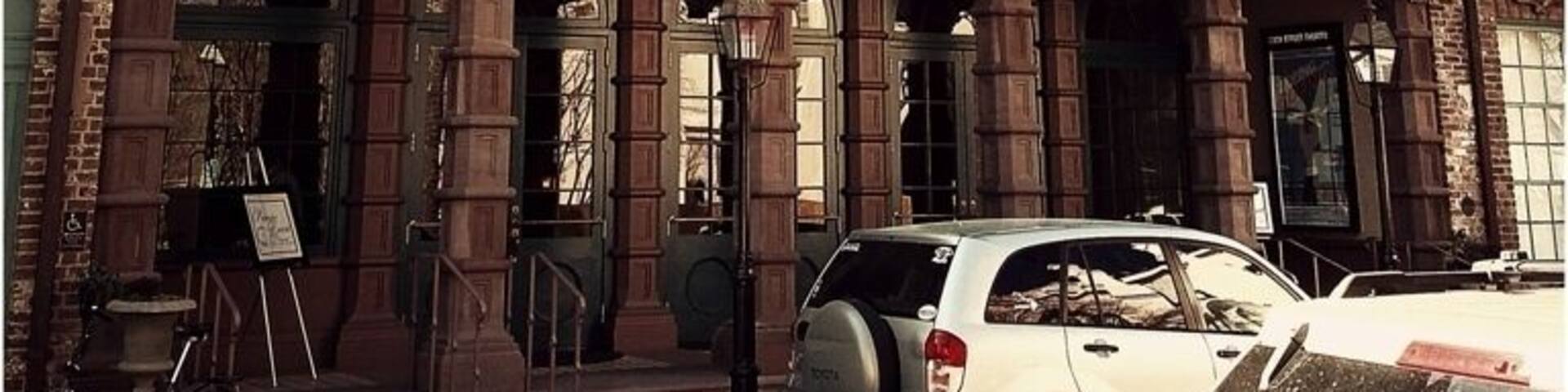 The Dock Street Theatre is Charleston's last surviving hotel from the antebellum period. The silhouette of its wrought iron balcony against the spire of St. Philip's church may be the single most photographed spot in the city. The main portion of the building was constructed around 1809 as Planter's Hotel. The hotel was built by Alexander Calder and his wife, who did so by renovating several pre-existing buildings at the site. The main entrance may not have been built until 1855 by J.W. Gamble.
The hotel was used extensively by planters from the midlands of South Carolina, who traveled to Charleston during horse-racing season. It was noted for its wonderful food and drinks during this era, and the South's famous Planter's Punch may have originated here. Guests to the hotel passed through the recessed porch with brownstone columns, into the lobby, and up a grand staircase that ascended to a drawing room. While much of the interior has been altered, these elements of the antebellum hotel remain and were adapted in subsequent uses of the building. A series of additions to the hotel throughout the 19th and 20th centuries can be easily identified by differences in brick coloration.
This theater is said to have been the first building built specifically for theatrical performances in America. Planter's Hotel occasionally housed one of the city's theatrical troupes, which performed at the nearby New Theatre during the mid-19th century. The most notable actor of this troupe was Junius Brutus Booth. Booth was the patriarch of an outstanding family of actors, which included John Wilkes Booth, President Lincoln's assassin. Junius Booth, who stayed at the Planter's Hotel, allegedly tried to kill his manager here in 1838. Today the Dock Street Theatre is home to the Charleston Stage Company, South Carolina's largest professional theater production company, and houses the city's Cultural Affairs office as well as The City Gallery, an exhibition space for local artists.