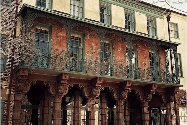 The Dock Street Theatre is Charleston's last surviving hotel from the antebellum period. The silhouette of its wrought iron balcony against the spire of St. Philip's church may be the single most photographed spot in the city. The main portion of the building was constructed around 1809 as Planter's Hotel. The hotel was built by Alexander Calder and his wife, who did so by renovating several pre-existing buildings at the site. The main entrance may not have been built until 1855 by J.W. Gamble.
The hotel was used extensively by planters from the midlands of South Carolina, who traveled to Charleston during horse-racing season. It was noted for its wonderful food and drinks during this era, and the South's famous Planter's Punch may have originated here. Guests to the hotel passed through the recessed porch with brownstone columns, into the lobby, and up a grand staircase that ascended to a drawing room. While much of the interior has been altered, these elements of the antebellum hotel remain and were adapted in subsequent uses of the building. A series of additions to the hotel throughout the 19th and 20th centuries can be easily identified by differences in brick coloration.
This theater is said to have been the first building built specifically for theatrical performances in America. Planter's Hotel occasionally housed one of the city's theatrical troupes, which performed at the nearby New Theatre during the mid-19th century. The most notable actor of this troupe was Junius Brutus Booth. Booth was the patriarch of an outstanding family of actors, which included John Wilkes Booth, President Lincoln's assassin. Junius Booth, who stayed at the Planter's Hotel, allegedly tried to kill his manager here in 1838. Today the Dock Street Theatre is home to the Charleston Stage Company, South Carolina's largest professional theater production company, and houses the city's Cultural Affairs office as well as The City Gallery, an exhibition space for local artists.