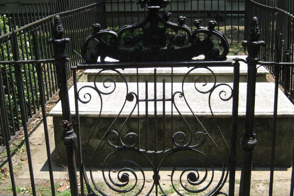 A wrought iron gate with intricate designs, a stone bench, and a building in the background.
