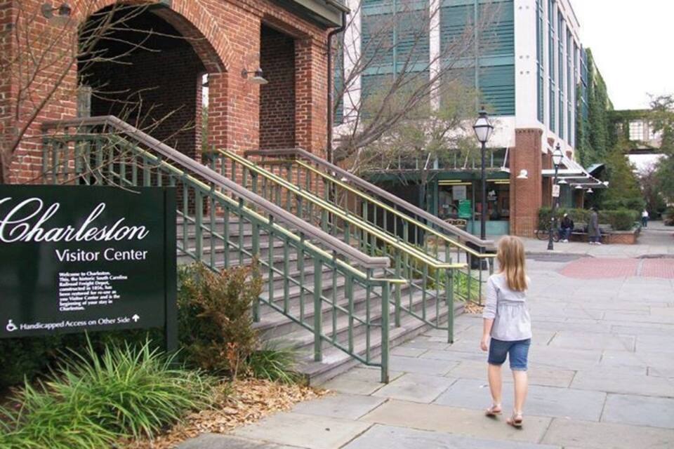 A brick building with a sign reading "Charleston Visitor Center" and a staircase leading up to it.