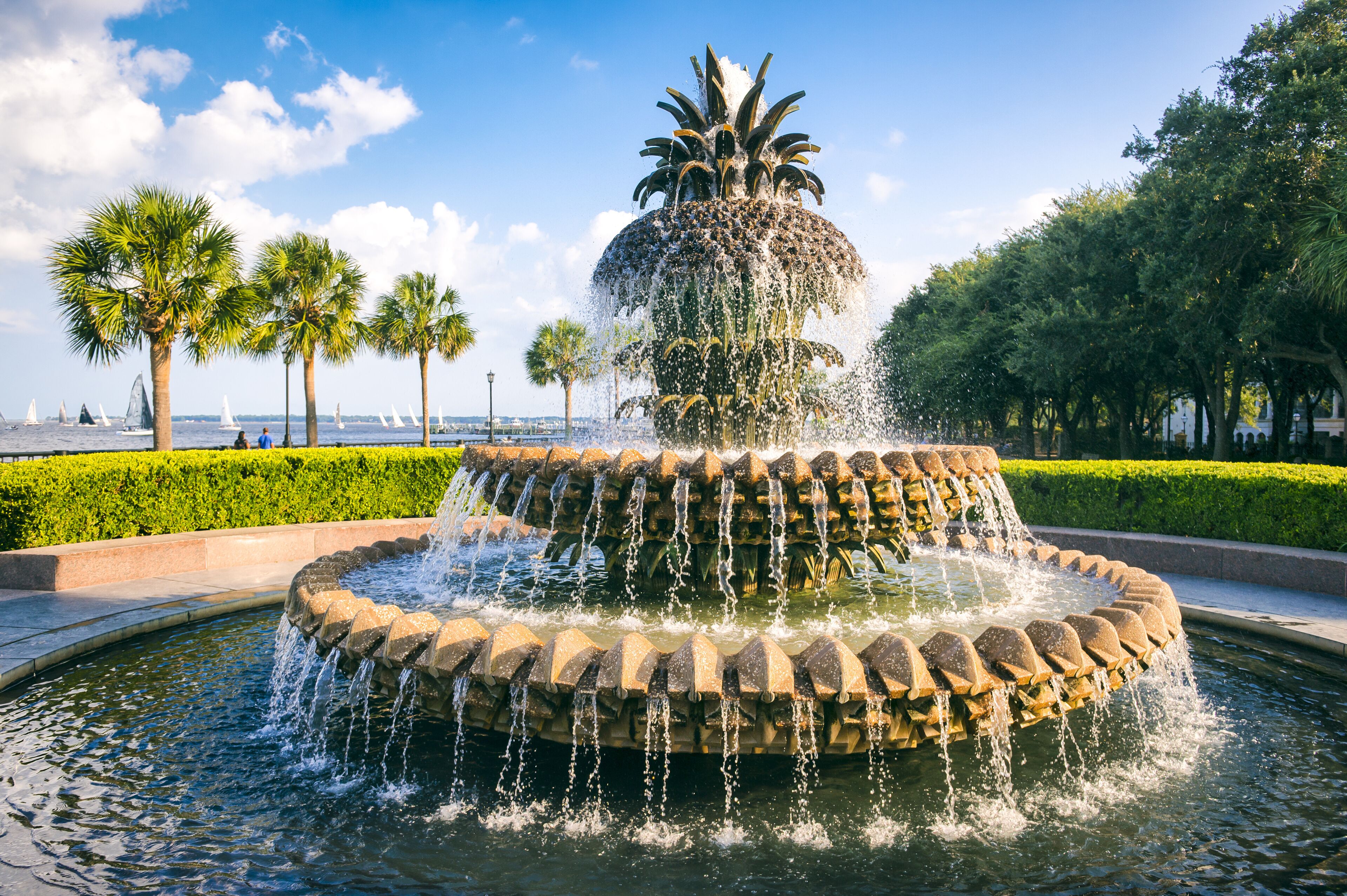 A multi-tiered water fountain with palm trees and a clear sky in the background.